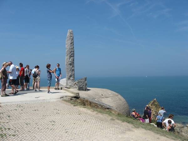 Tourists beside a stone monument atop the Pointe du Hoc promontory