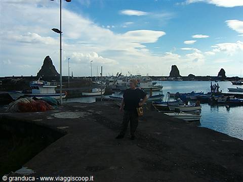 Man on the pier of Acitrezza harbor, boats and basalt sea stacks