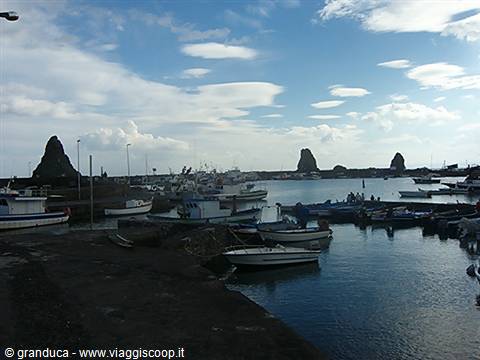 Fishing boats moored at Aci Trezza harbor with the Faraglioni sea stacks