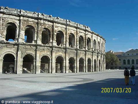 The ancient Roman amphitheater of Nîmes with stone arches under blue sky