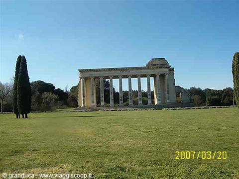 Stone colonnade monument in a park, green lawn, cypress trees, bright light