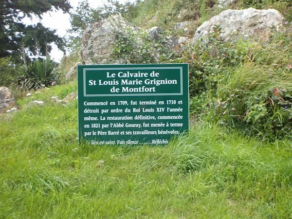 Green sign of the Calvaire de Saint-Louis-Marie Grignion de Montfort among grass and rocks