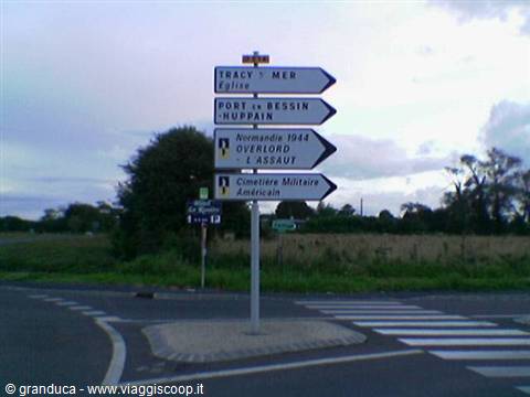 White road signs point to the Normandy American Cemetery near Colleville