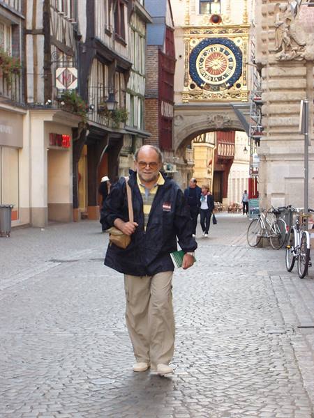 Man walks on cobblestones of rue du Gros-Horloge in Rouen, golden clock behind