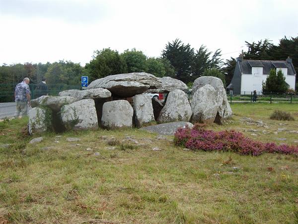Megalithic stone dolmen among grass and heather, tourists walking, overcast sky