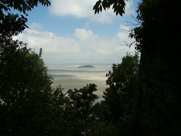 Sandy bay with Tombelaine islet framed by trees and a stone wall