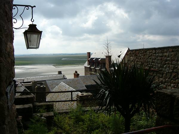 Wrought-iron lantern on stone wall, slate roofs and bay under cloudy sky