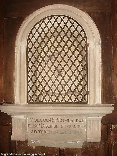 Ancient stone millstone of Saint Romuald behind metal grate on marble shelf