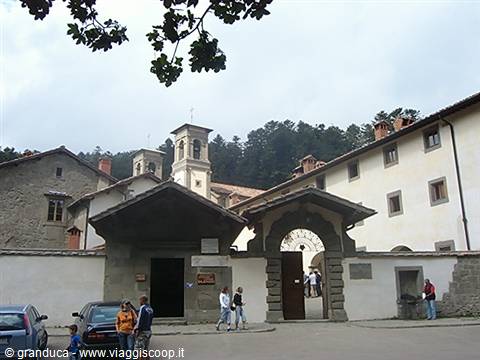 Monastery with bell tower and arched gate, visitors walking in the entrance courtyard