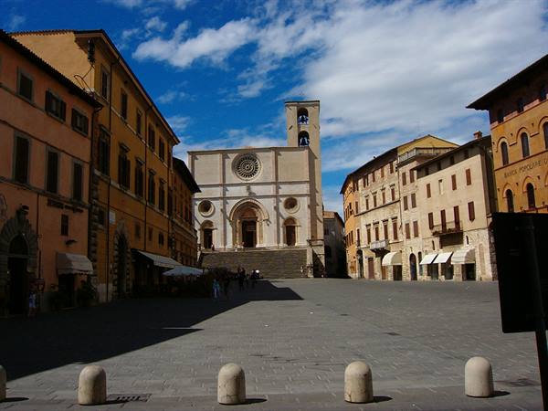 Stone cathedral with rose window overlooking a cobblestone square between ochre buildings
