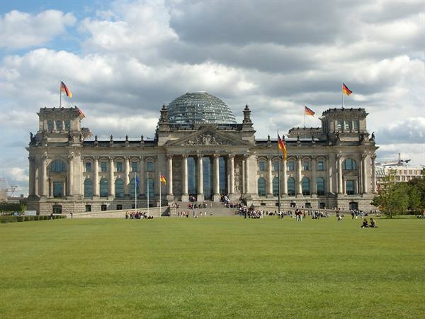 The Reichstag in Berlin with its glass dome, visitors on the lawn under clouds