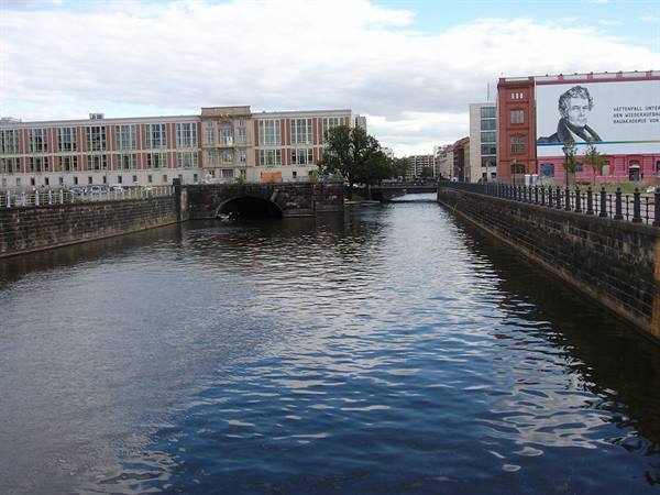 Stone-lined canal flanked by historic buildings under a cloudy sky in Berlin