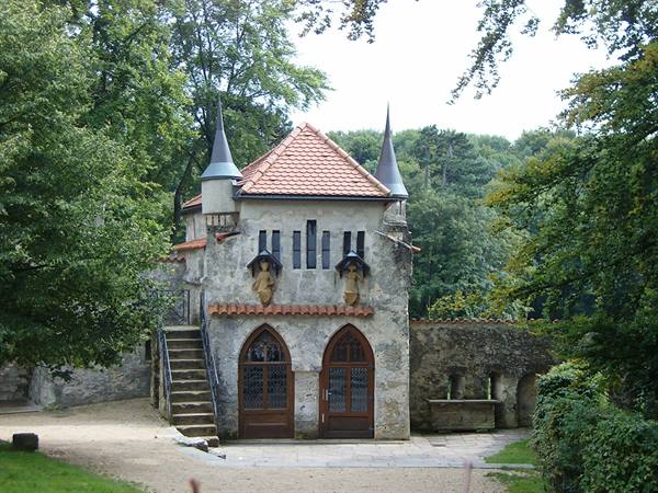 Small stone chapel with red tile roof and spires among green trees