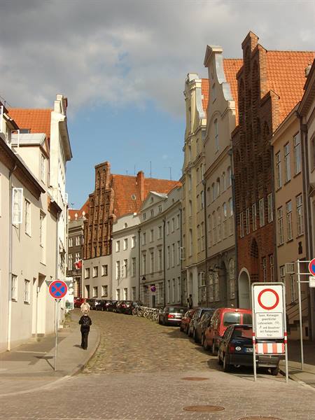 Cobblestone street in Lübeck, brick gabled houses, parked cars, lone pedestrian