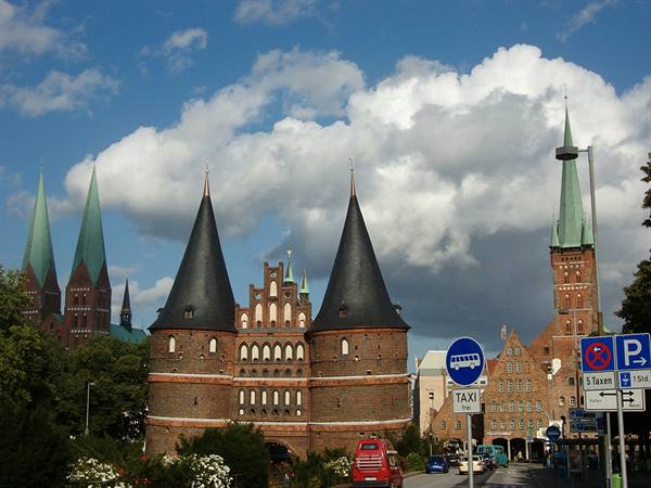 Brick Holstentor gate in Lübeck under white clouds, street traffic below