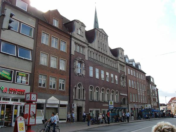 People and bicycles in front of brick buildings with pharmacy and bus shelter
