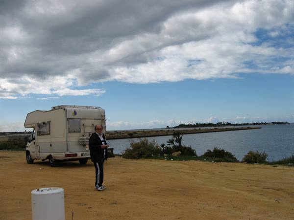 Motorhome parked on sand by the lagoon, man walking under heavy clouds