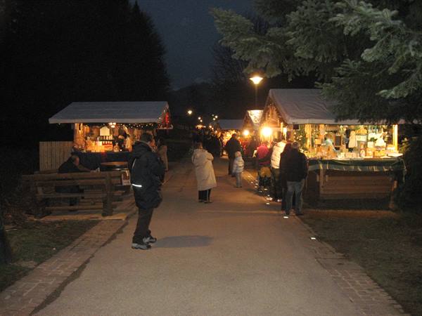 Evening Christmas market with illuminated wooden stalls, visitors walking the path