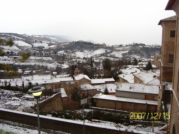 Snow-covered rooftops and bell tower among hills under gray winter sky