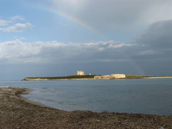 Rainbow over Isola delle Correnti, stone buildings by the sea