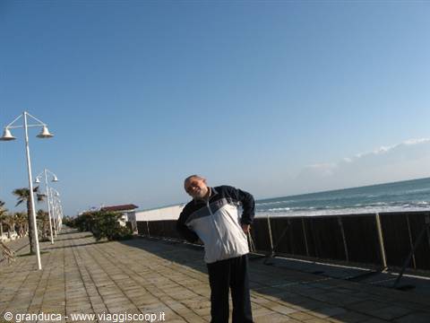 Smiling man in sport jacket on paved seaside promenade by the waves