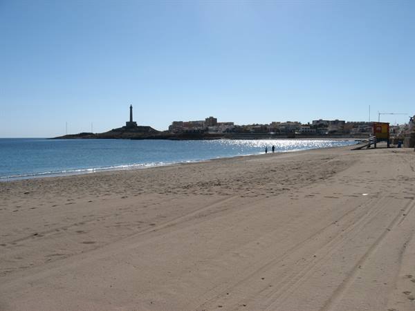 Sandy beach facing the Cabo de Palos lighthouse, white houses and sparkling sea