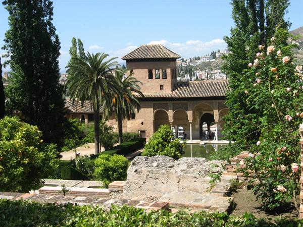 Brick tower with arcades over a pool, palms and roses at the Alhambra, Granada