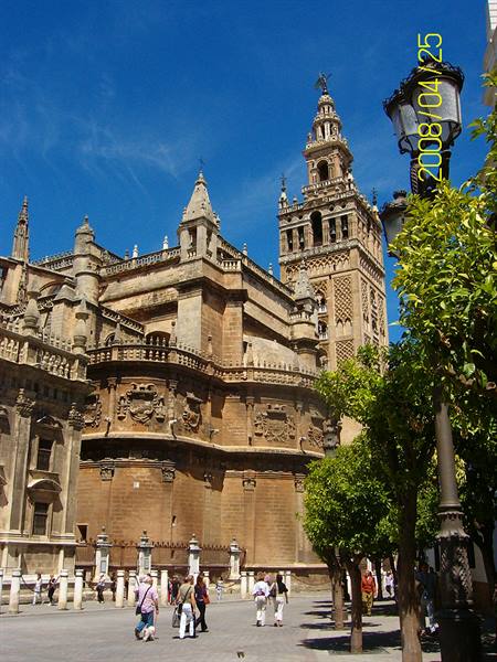 The Giralda and Seville Cathedral under blue sky, tourists walk among orange trees