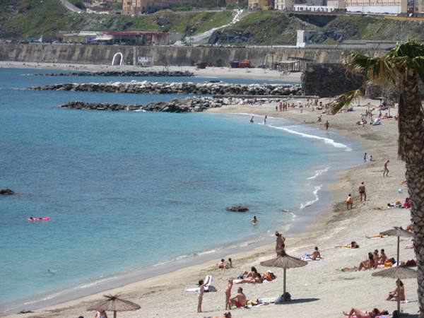 Beach with swimmers, straw umbrellas, palm tree and rocky breakwaters