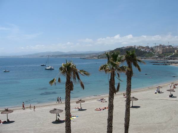 Palm trees on sandy beach with umbrellas, swimmers and boats in blue sea