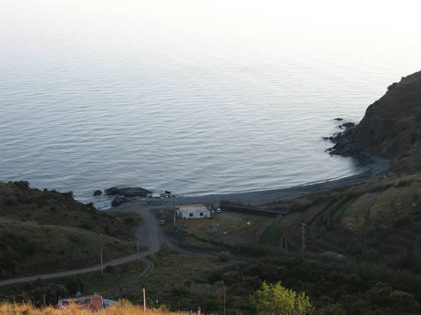Cove with pebble beach and white houses between dark green hills