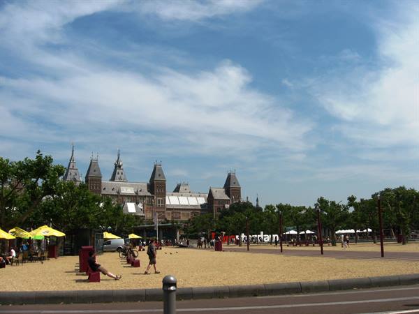 Rijksmuseum building in Amsterdam with red sign and tourists under cloudy sky