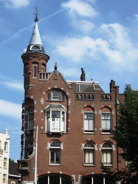 Red brick building with conical turret and arched windows under blue sky