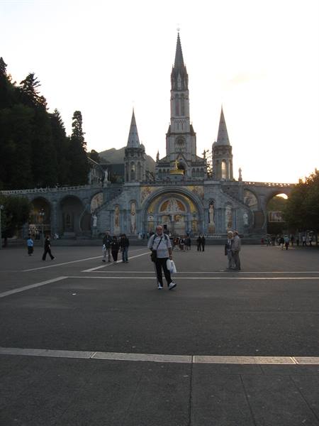 Pilgrims walking across the plaza in front of the Lourdes basilica at dusk