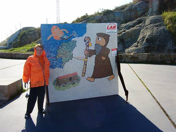 Woman in orange jacket beside pilgrim mosaic mural on rocky plaza