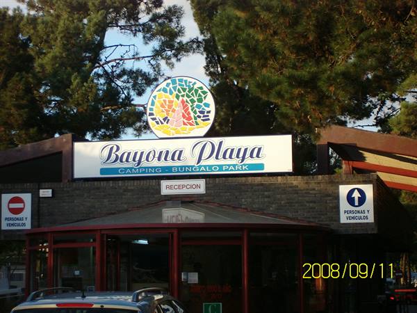 Bayona Playa campsite entrance, bright sign above the reception among pine trees