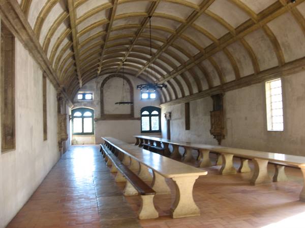 Refectory with wooden vaulted ceiling, long stone tables and benches under window light
