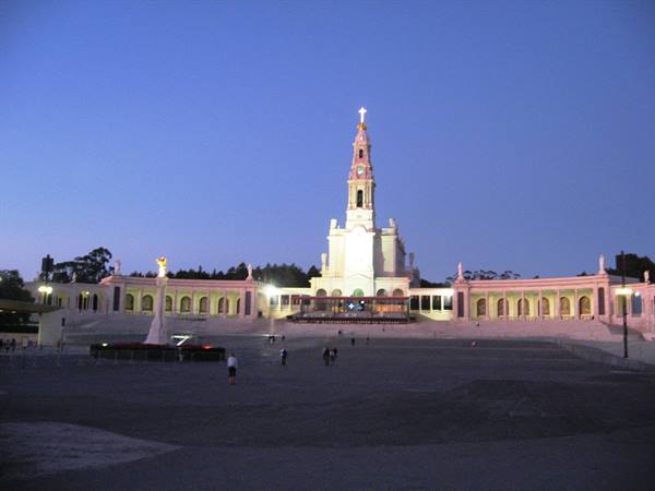 Fátima Sanctuary lit at dusk, pilgrims walking across the large square