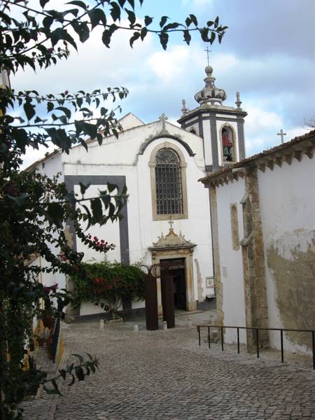 White church with bell tower framed by branches, cobbled alley