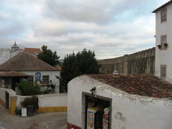 Medieval stone walls in Óbidos, whitewashed houses with terracotta roofs under cloudy sky
