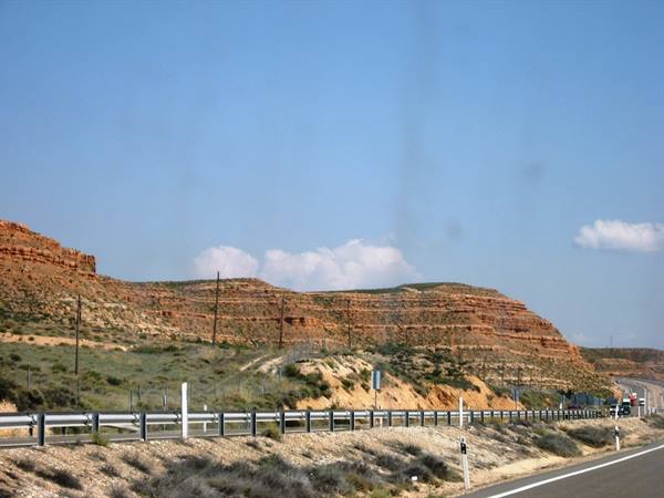 Highway with guardrail in front of red rocky hills and dry shrubs