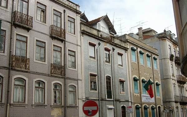 Old buildings with wrought iron balconies and Portuguese flag under grey sky