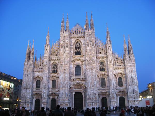 Milan Duomo's marble Gothic spires glowing at dusk, crowds filling the square