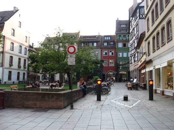 Pedestrian square with colorful half-timbered houses, parked bicycles and people sitting on low walls