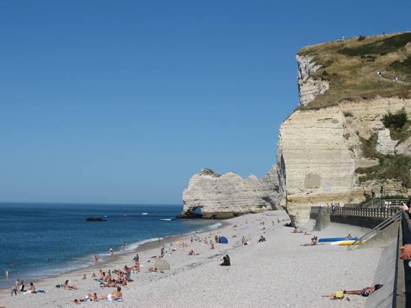 Beachgoers on pebble beach beneath white chalk cliffs of Étretat