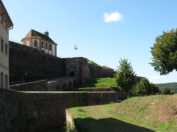 Stone church atop a fortified citadel wall, French flag flying under blue sky