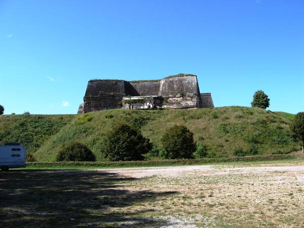 Stone fortress atop grassy hill, blue sky, camper van parked below
