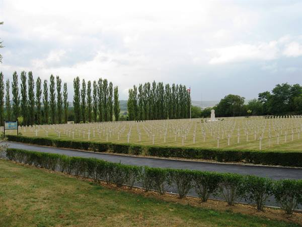 Military cemetery with white crosses in rows, tall poplars and cloudy sky