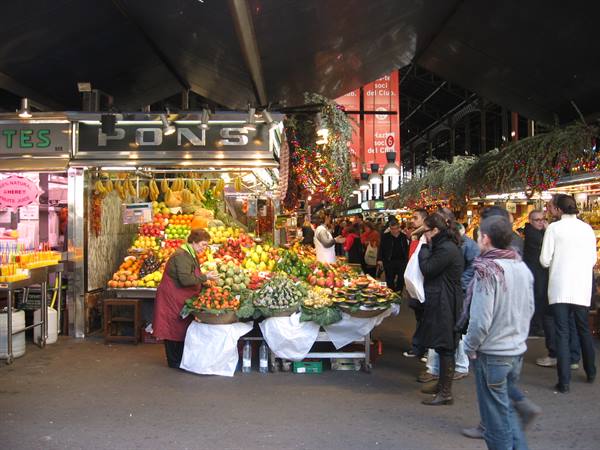 Fruit stall at Mercat de la Boqueria, vendor in red apron among the crowd