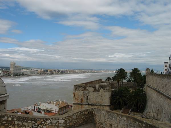 Ancient fortress walls of Peñíscola above palms and beach under clouds